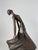 This modern bronze sculpture captures a stylized female figure in motion, her flowing dress sweeping outward as if caught...