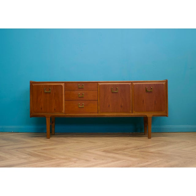 A stylish teak sideboard by Nathan Furniture, featuring three central drawers, twin cupboards and raised tapered legs. The...