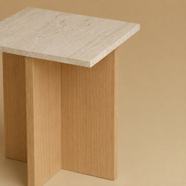 Two materials, one line. The Tinos is a small, low table scaled for the side of a bed, its travertine surface carried on a...