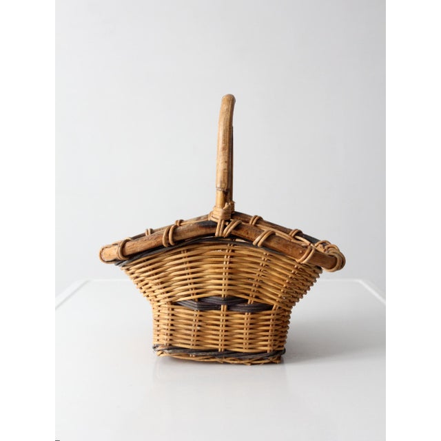 Vintage gathering basket with a softly flared form and an upright handle, woven in warm natural tones with darker accents...