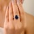 This elegant engagement ring features a stunning 5-carat oval-cut deep blue sapphire as the centerpiece, securely held by...