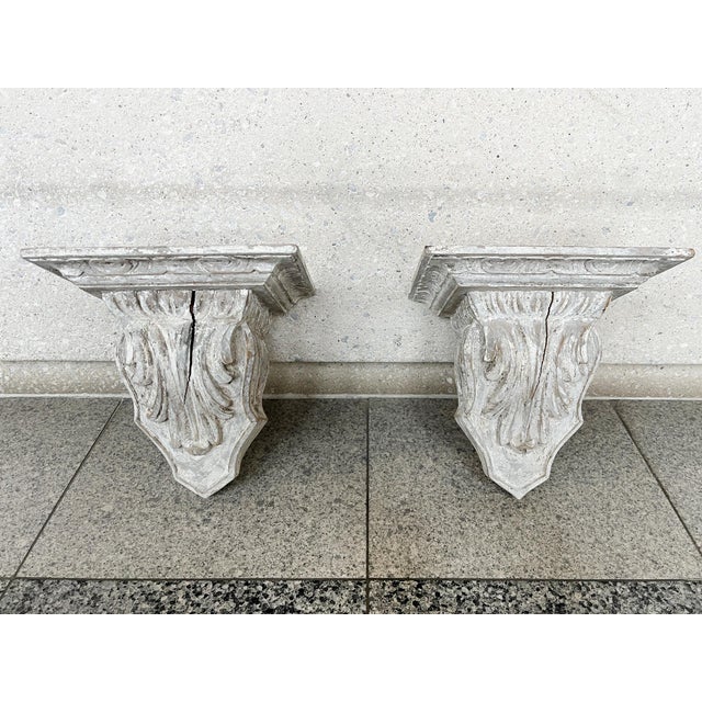 Pair of antique decorative wood brackets, hand-painted white. Carved acanthus leaves decorate the front crest, while a...