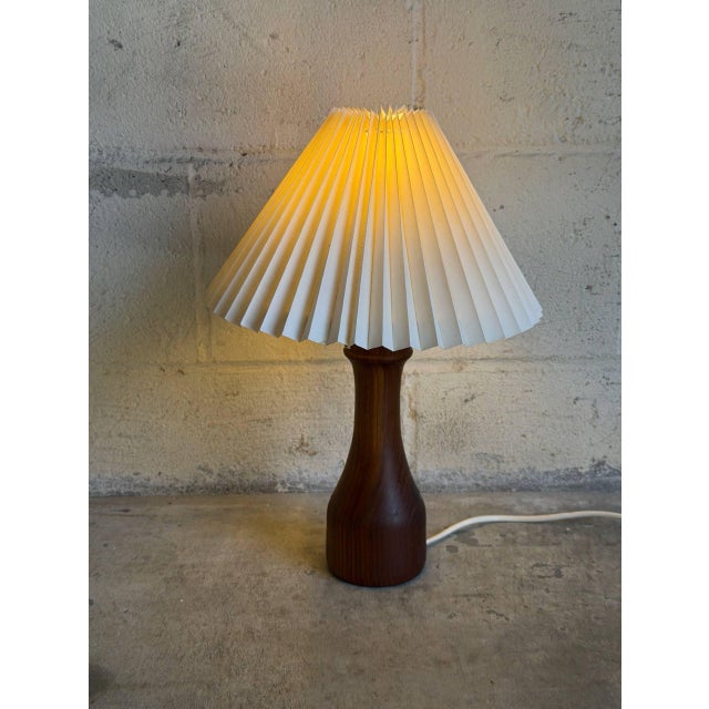 A turned sculptural teak base pairs with a pleated beige shade for an organic silhouette. Soft diffused light enhances its...