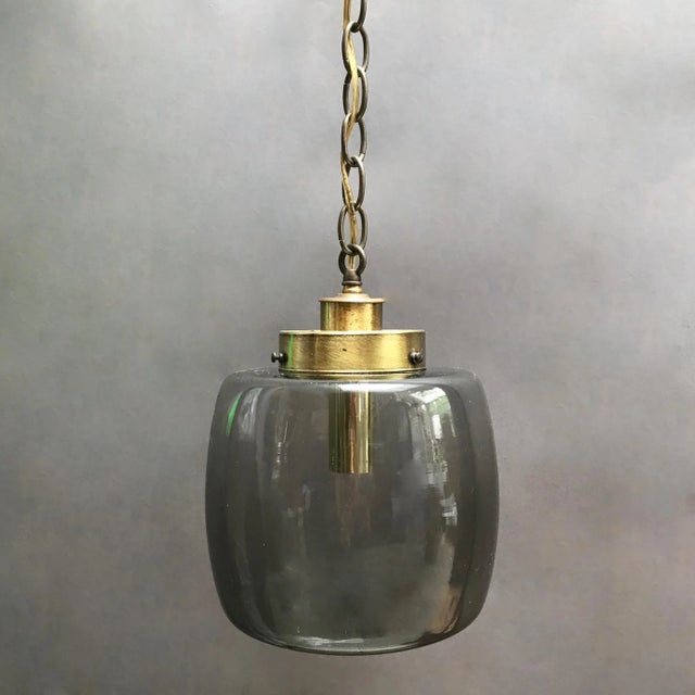 Mid-Century Modern, pendant light features a smoked glass closed lantern shade with brass fitter and 44 inches of brass...