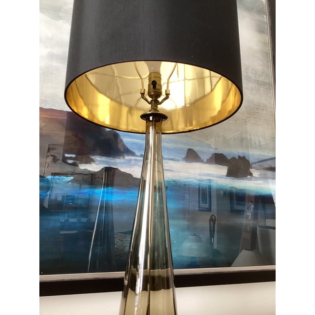 Elegant vintage table lamp featuring a tall, tapered form in smoky amber glass, anchored by a brass base and accented with...