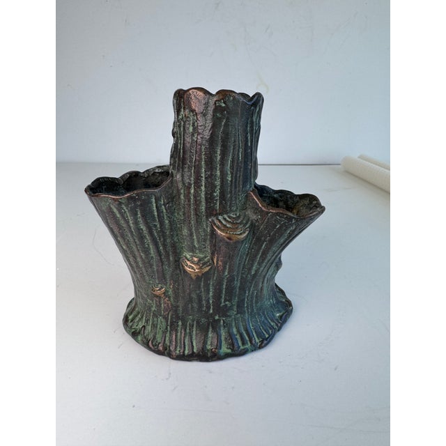 A metal vase with green patina. There are three openings for flowers and a place for a candle.