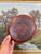 This vintage hand-hammered copper plate features a warm red patina with areas of dark oxidation and age-related wear. The...