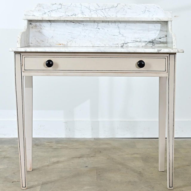 This 19th-century English vanity table features a white marble surface atop a recently painted wooden frame. The vanity...