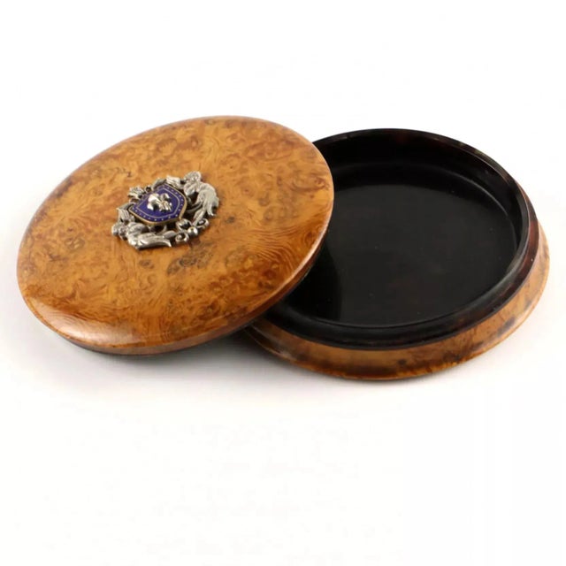 A round box of wavy birch and tortoise shell , with a silver coat of arms and a royal lily on the blue enamel of the...