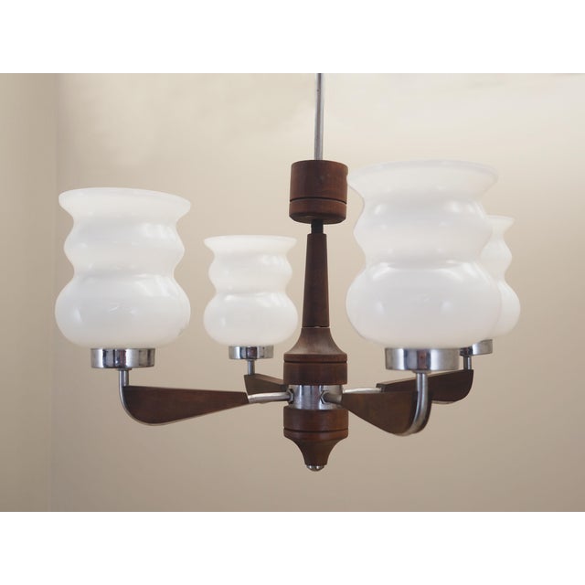 The chandelier was made in the 1970s, Danish production. Made of wood, metal and glass. The glass is white in colour....