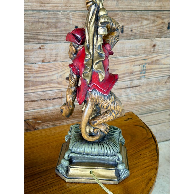 A delightful pair of figural monkey lamps by Wildwood featuring mischievous monkeys dressed in vibrant red attire and...