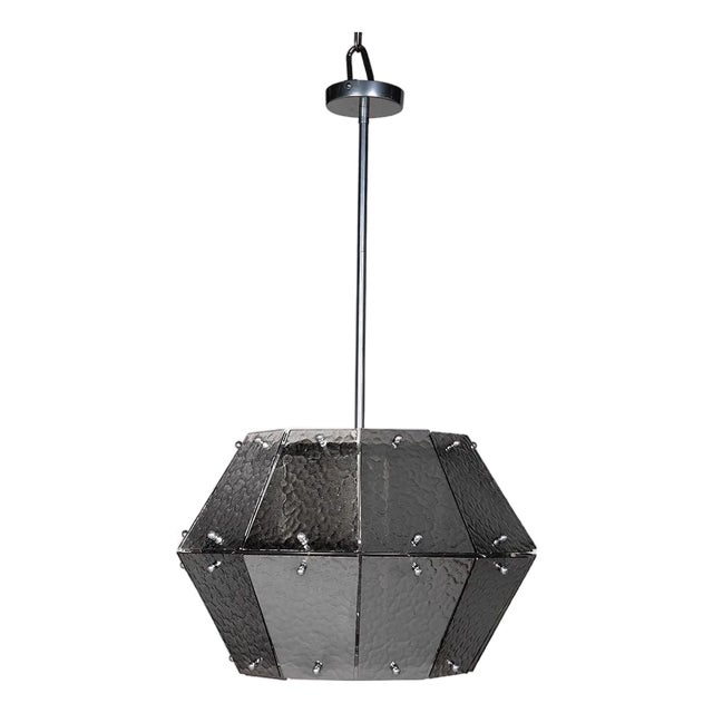 A geometric chandelier featuring hammered smoked-glass panels and polished metal suspension. When unlit, it maintains a...