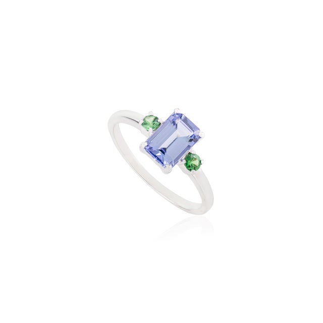 This refined, contemporary three-stone ring features an emerald-cut center tanzanite flanked by round-cut tsavorites,...