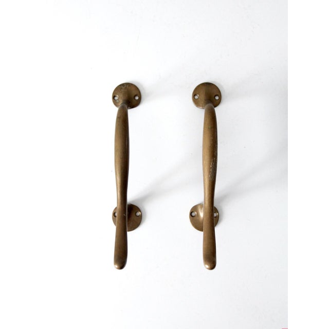 This is a pair of vintage brass door handles. The classic door pulls have a sweeping, sleek design with holes on the bases...