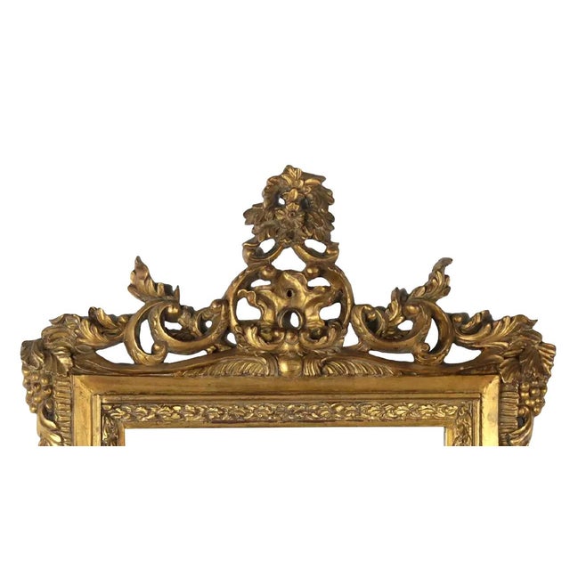 The top of the frame features a striking scroll crown, with carved leaves extending outwards from the center to form a...