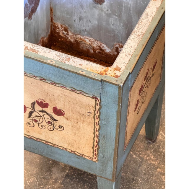 A cheerful painted cellaret converted to use as a planter, in powder blue with folk-painted panels on each face depicting...