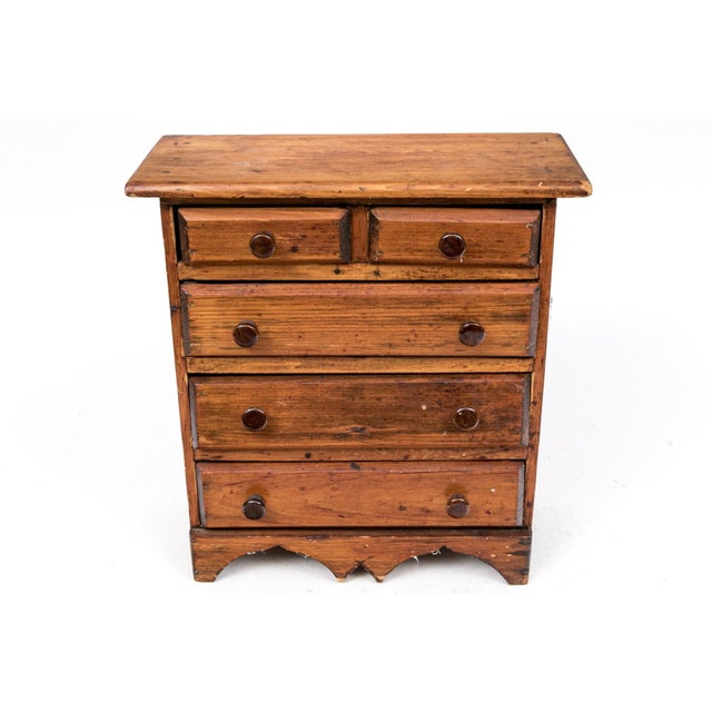A small antique pine chest of drawers with two short top drawers, three graduated long drawers, dark stained turned wood...