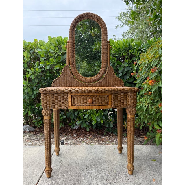 A charming vintage wicker and rattan vanity featuring an oval swivel mirror, single storage drawer, and beautifully...