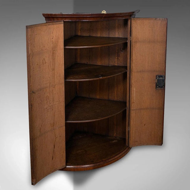 This is an antique bow front corner cabinet. An English, mahogany and oak wall mount cupboard, dating to the Georgian...