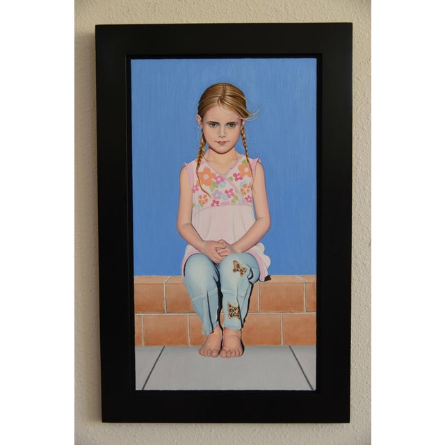 The artwork presents a young girl seated against a vibrant blue background, her posture conveying a sense of...