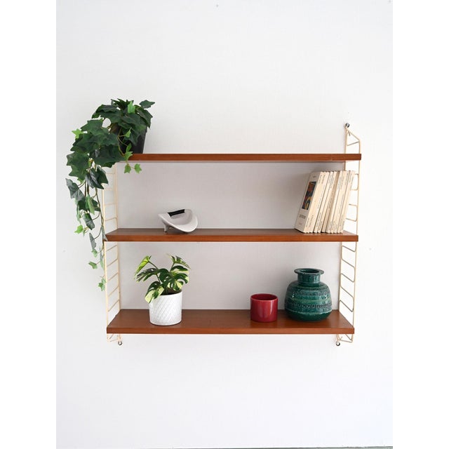 Wall system with three adjustable teak shelves and white lacquered metal side structure. Hylla wall system of Scandinavian...