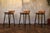 A sophisticated set of three mid-century modern bar stools, dating to the 1960s, distinguished by their clean...