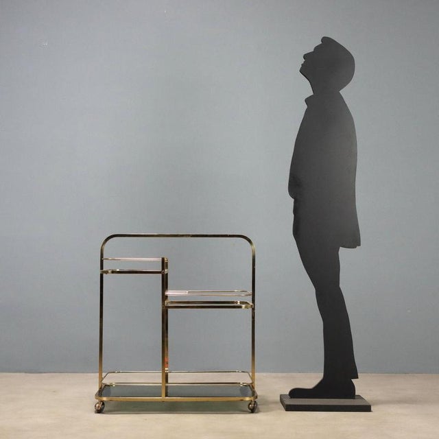 1970s bar cart with a brass frame, featuring smoked glass shelves that add elegance and functionality. Equipped with a...