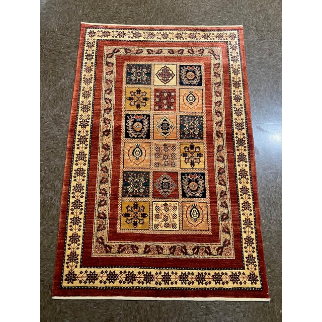 Hand-knotted Persian Kashkoli wool rug featuring a red field with a central grid of square panels, each containing...