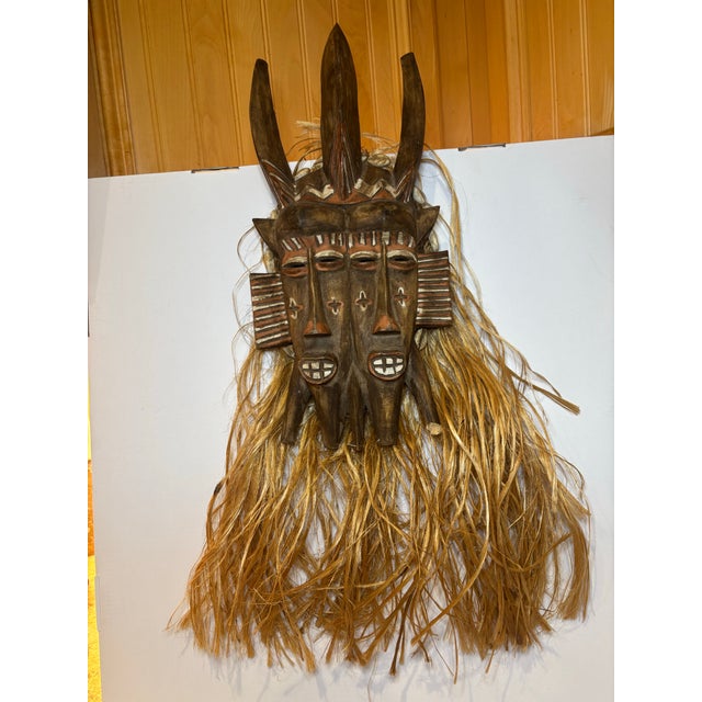Hand-carved West African mask featuring a striking double-faced form, tall vertical horned elements, and an integrated...