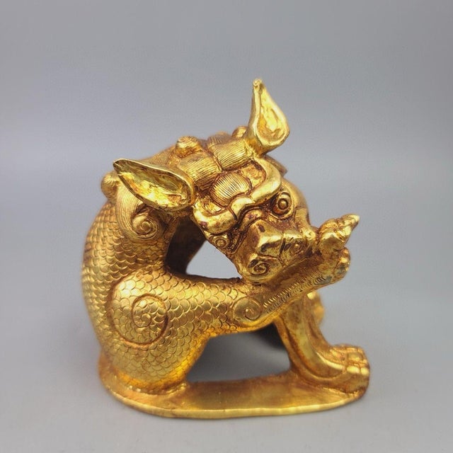 This finely cast gilt bronze sculpture depicts a Qilin, a mythical hooved creature from traditional folklore, in a seated,...