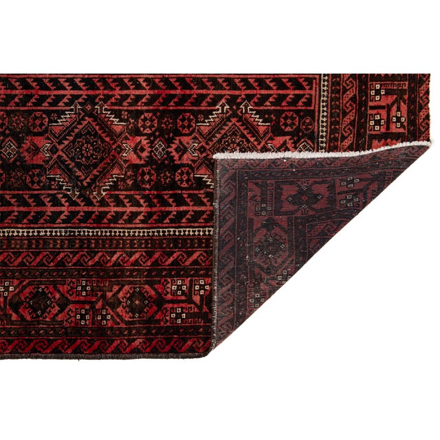 This striking vintage Persian Baluch rug features a deep, moody palette of madder red, espresso brown, and charcoal black....
