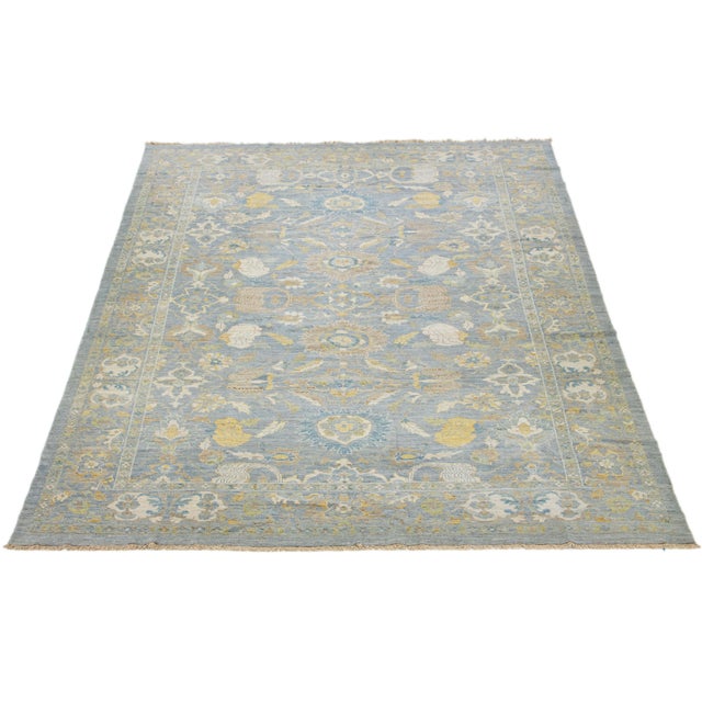 This hand-knotted wool rug has a light blue background adorned with brown and yellow accents in an all-over design. This...
