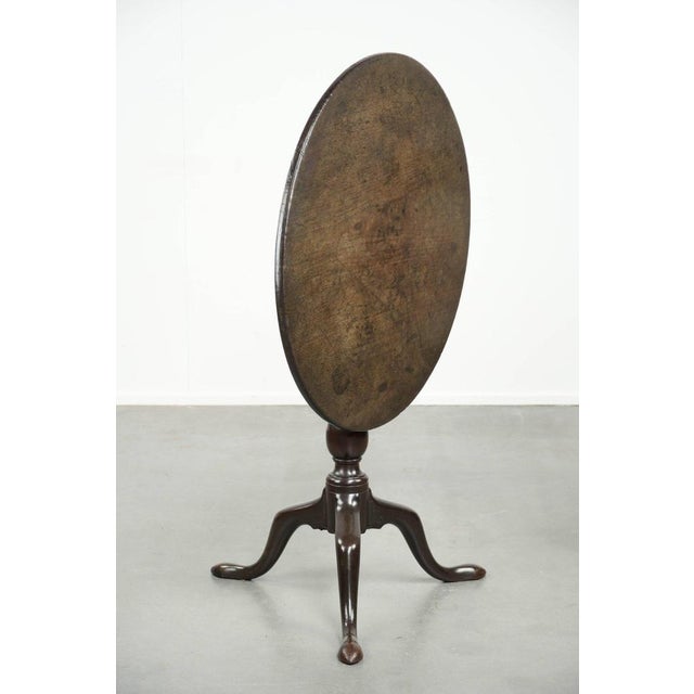 This elegant and practical round antique English tilt-top table from the 18th century features a luxurious, warm color and...