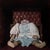 This oil on wood panel features a lifeless figure dressed in a pale blue gown, evoking a sense of eerie stillness and...