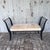 A striking vintage bench with a black iron frame accented in warm brass trim along the curved, saber-style legs and...