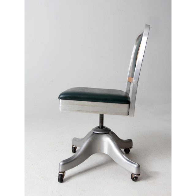 This mid-century modern Shaw-Walker swivel desk chair features an aluminum base with casters, a curved wood back, and a...