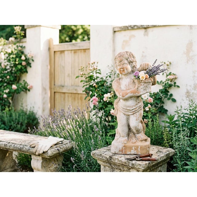 A French terracotta garden statue of a cherubic child holding a flower basket. Good condition with fading white paint and...