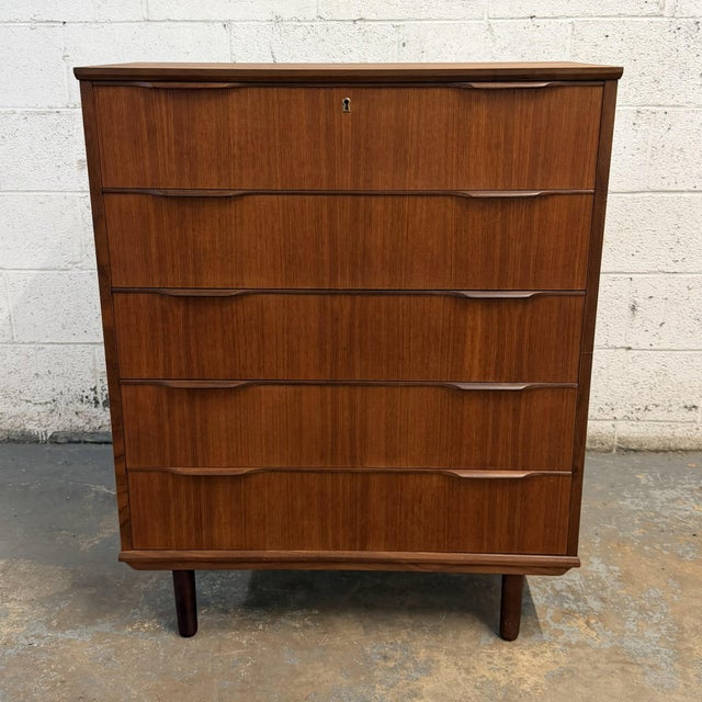 A Danish teak five-drawer chest by Ejsing Møbelfabrik, dating to the 1950s. The piece has a clean, compact form with warm...