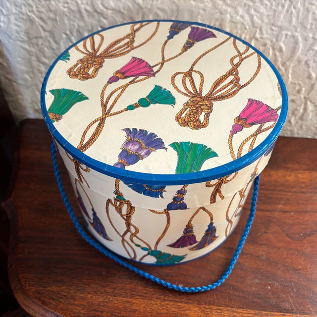 Vintage 1990s cardboard hat box with tassel motif and blue rope handles. Please see condition details noted. Most items...