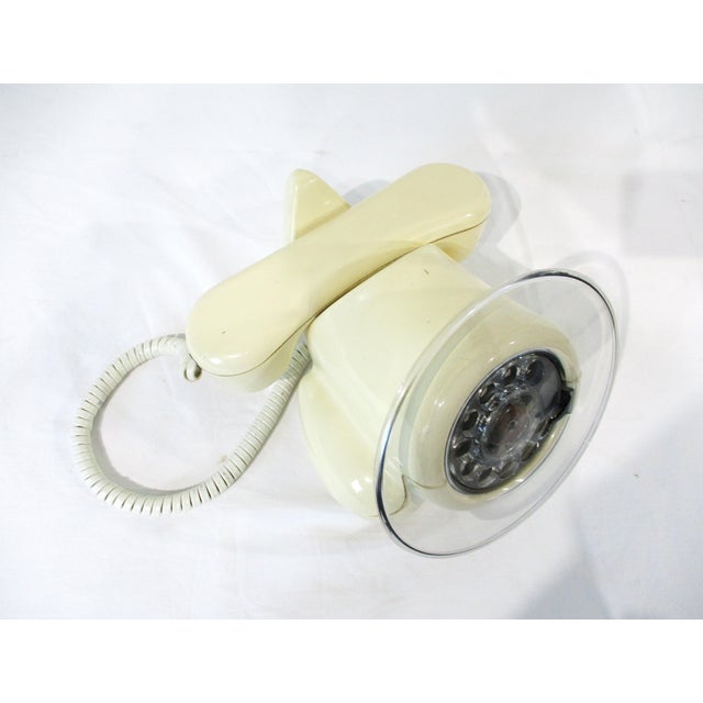 A telephone designed in the manner of an early airplane with rotary dial to the front and a clear Lucite ring making it...