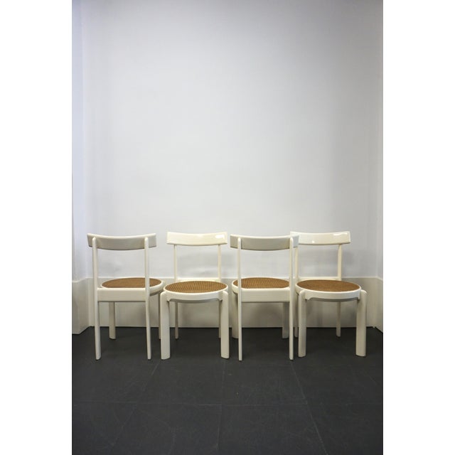 Set of four white lacquered wooden chairs with cane seats. An Italian design from the 1970s. The interplay of the leg...