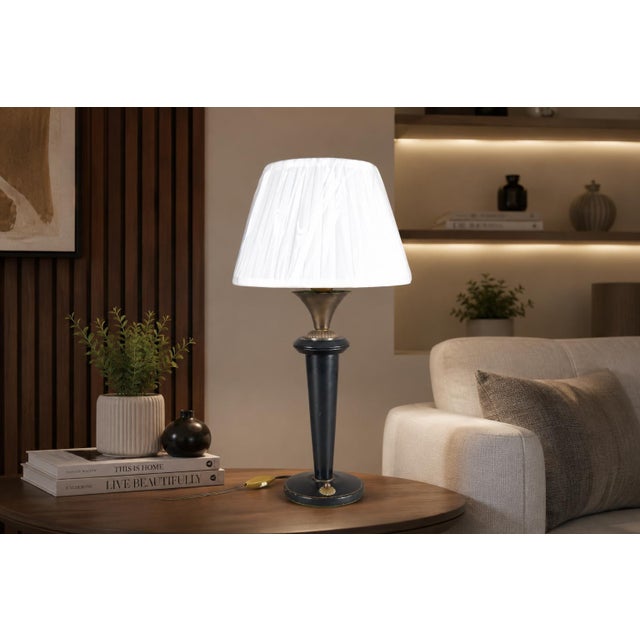 Table lamp dating to the 1950s, with a tall tapered metal column wrapped in navy blue leather. Brass accents at the top...
