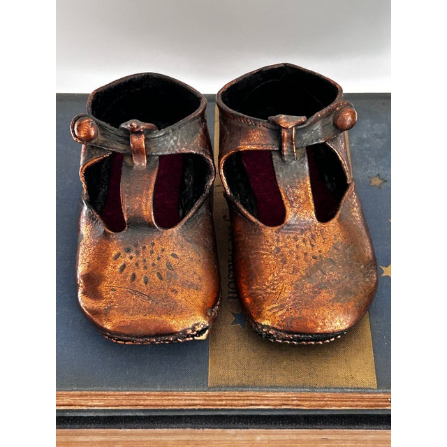 A charming pair of vintage copper-plated miniature baby shoes in a classic Mary Jane silhouette. These early 20th-century...