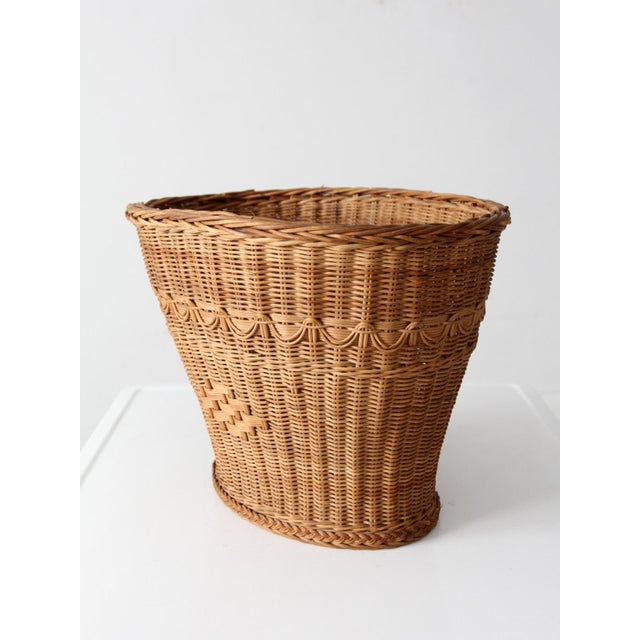 This vintage woven basket features a warm honey tone with a gently flared shape and scalloped trim. It is accented with a...