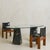 An Italian dining table from the 1970s, composed of a thick oval glass top set on two sculptural Nero Marquina marble...