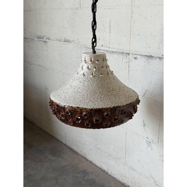 Featuring a flared shade with heavy relief texturing and perforated cutouts along the body, this pendant light provides...