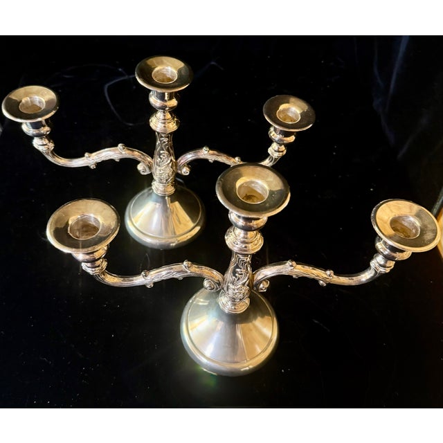 This set features a pair of elegant, multi arm silver-plated candelabras reflecting a distinct mid-century French...