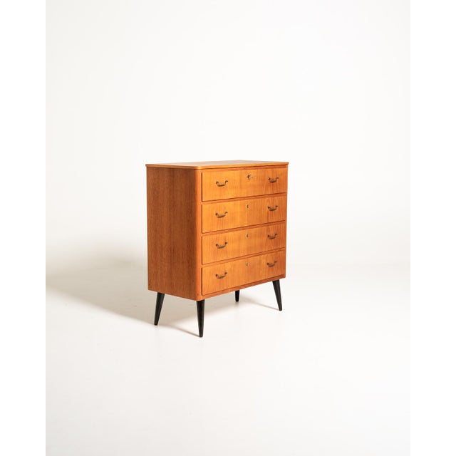Scandinavian teak chest of drawers with four large drawers, brass handles, and tapered black lacquered legs, 1950s/1960s....