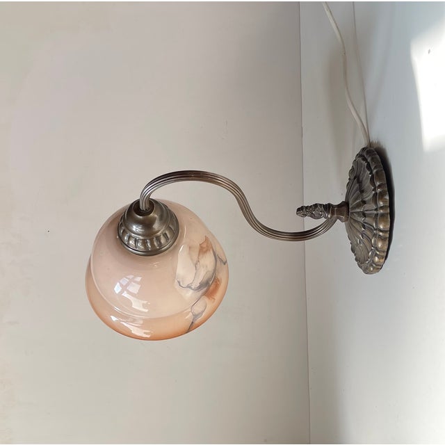 Sculptural wall light featuring a salmon colored marble glass shade and a brass base sculpted with stylized leaves. It was...