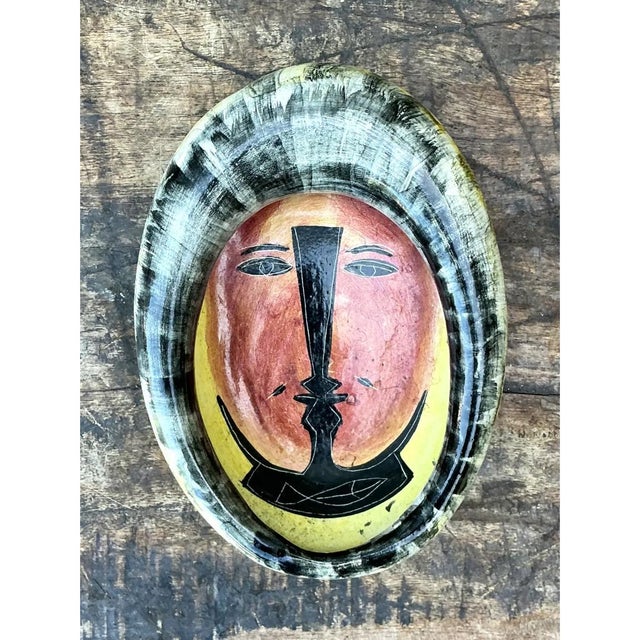 This decorative bowl presents an oval, deeply cupped form, its interior serving as a graphic canvas for a bold, stylized...
